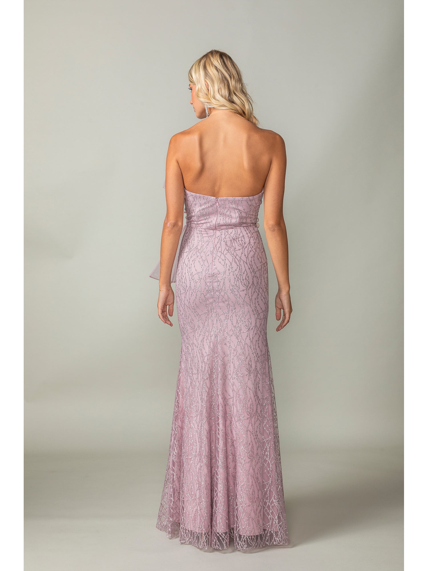 A woman faces away, wearing the Side-Bow Strapless Long Glitter Prom Dress 4394 featuring a fitted bodice and flared hem in shimmering light purple, set against a plain background.