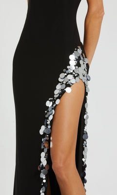 A person wearing the Long Formal Dress 44037 by Mac Duggal, a black fitted gown with a high slit, large silver sequins, and an open back that showcases the torso and legs.