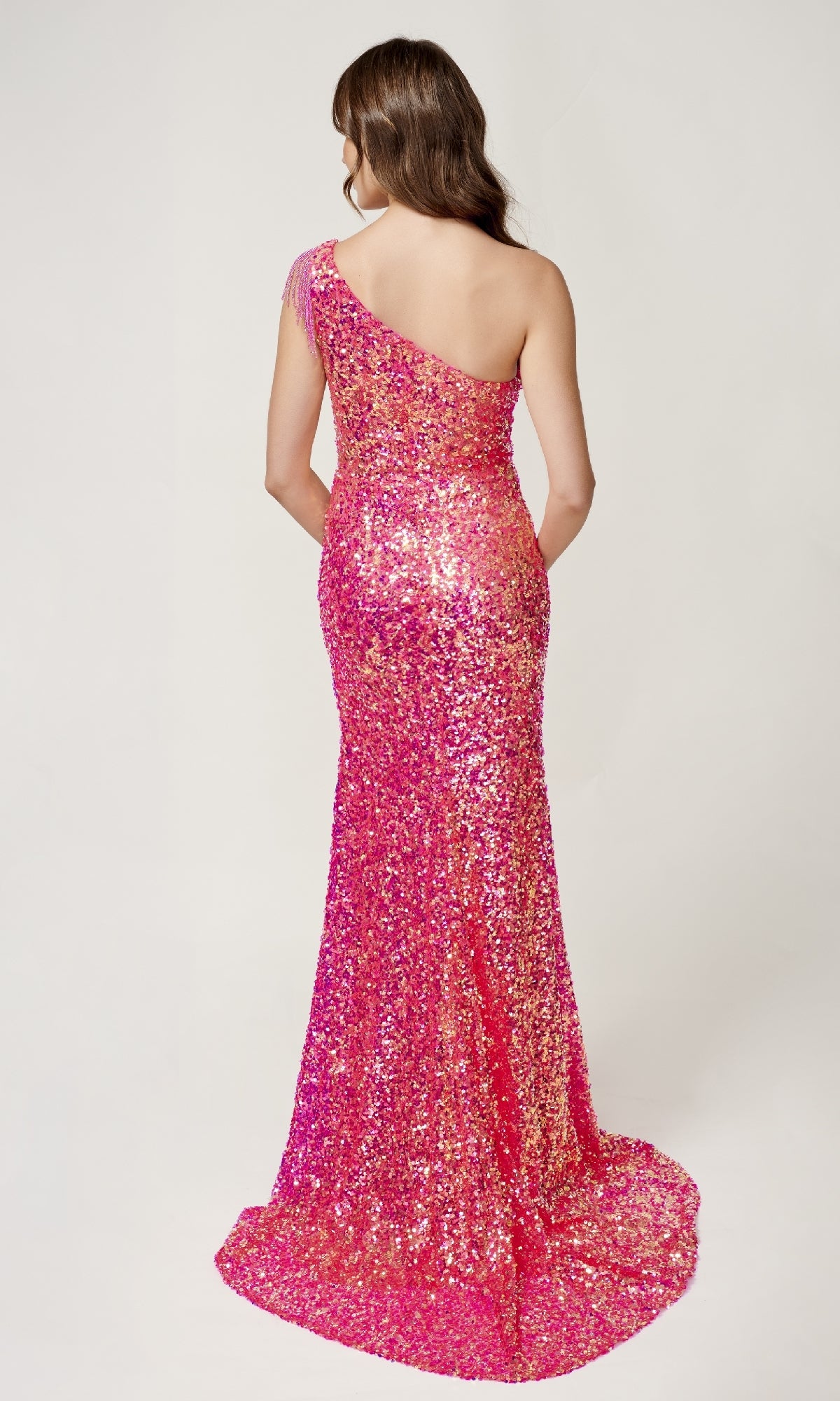 A woman faces away, modeling the Nina Canacci 4405 Sequin Prom Dress—floor-length, pink, fitted silhouette with a one-shoulder neckline—against a plain white background.