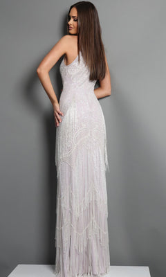 A woman stands on a white platform wearing the Jovani 44061 long formal dress, a fitted white gown featuring intricate beading and Art Deco fringe detailing, facing away with her head turned slightly to the side.