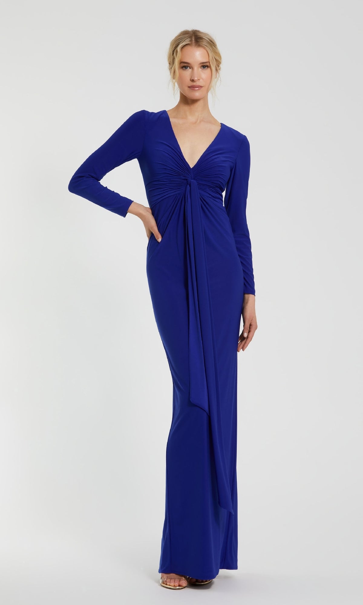 A woman poses against a plain light background, wearing the Mac Duggal 44064 blue long sleeve formal dress featuring a deep V-neck and front draping detail.