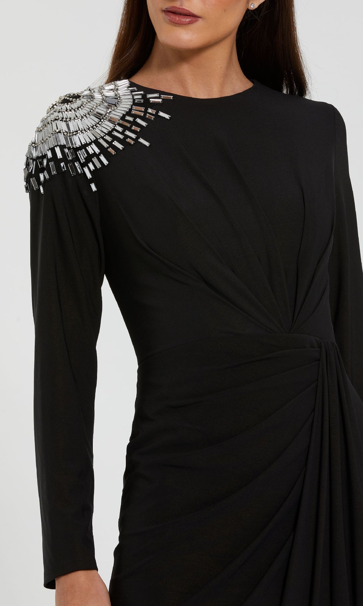 A woman wears the Mac Duggal 44136 long formal dress in black, featuring a gathered waist and striking silver crystal beading in geometric shapes on one shoulder.