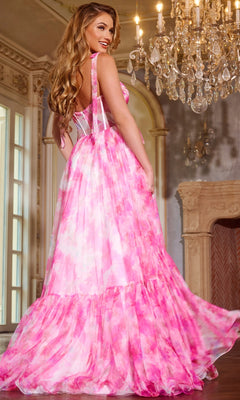 A woman wearing the Watercolor-Print Pink Prom Gown by Jovani 44181 stands indoors near a chandelier and ornate fireplace, looking over her shoulder with a smile.