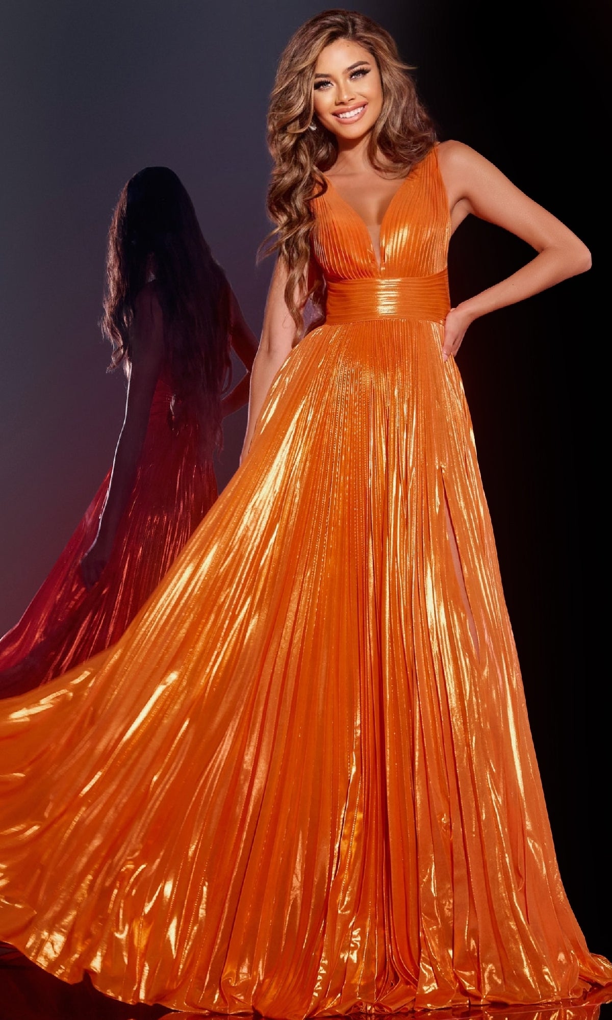 A woman stands smiling with one hand on her hip, wearing the Jovani 44230 long sleeveless orange prom dress featuring a deep V-neckline and elegant A-line skirt; her reflection appears in the background.
