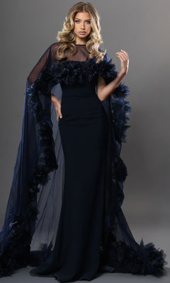 A woman wearing the Jovani 44321 Long Formal Dress—a fitted, floor-length navy gown featuring sheer cape-like sleeves adorned with dark floral accents—stands against a gray backdrop.