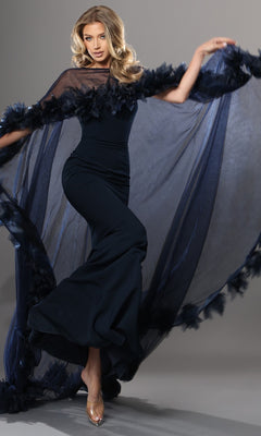 A woman poses gracefully against a plain grey backdrop wearing the Jovani 44321 long formal dress in navy, featuring a fitted silhouette and a sheer, flowing cape.