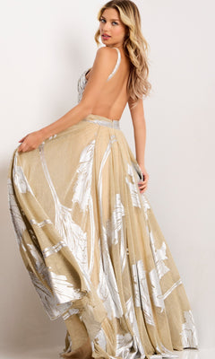 A woman poses sideways in the Jovani 44421 long prom dress—a backless gold and nude gown with silver metallic leaf accents—holding the flowing skirt and glancing over her shoulder against a simple light background.