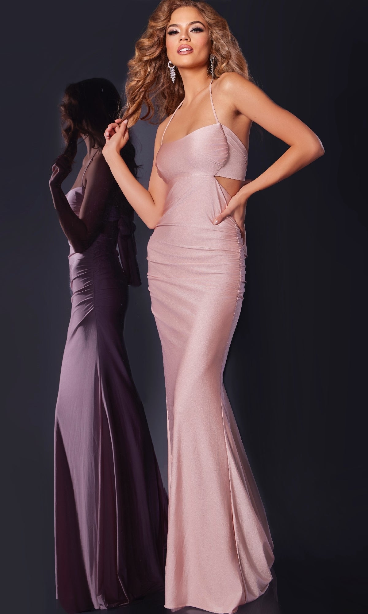 Wearing the Jovani 44513 long prom dress featuring thin straps, side cut outs, and an elegant open back, a woman poses against a dark background with her reflection visible.
