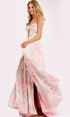A woman smiles in the Jovani 44518 long prom dress, holding the side of her flowing pink/print chiffon skirt to show its movement—an elegant strapless floral gown perfect for prom.