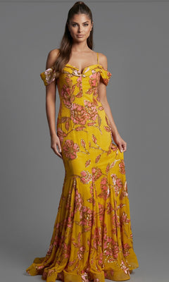A woman wearing the Long Formal Dress: Jovani 44652—a yellow gown with pink floral embroidery—stands against a plain gray background.