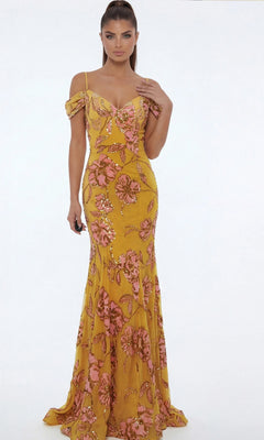A woman models the Jovani 44652 long formal dress, featuring a yellow base with pink floral patterns, as she stands against a plain white background facing forward, one hand at her side and the other touching her hair.