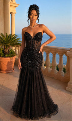 A woman in the black Sequin-Bodice Long Prom Dress (Dancing Queen 4468) stands on a terrace with balustrades, a potted palm, and an ocean view at sunset.