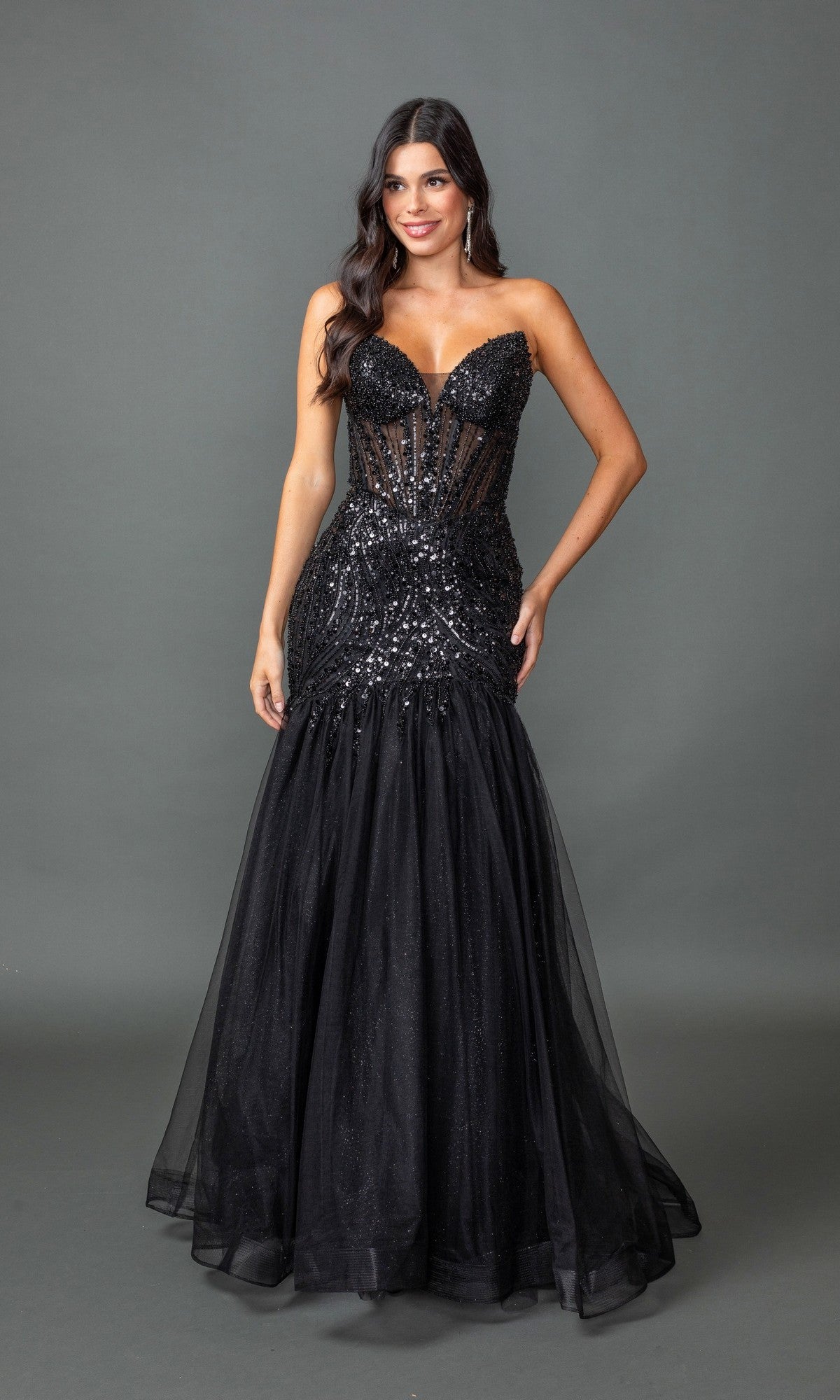 A woman stands against a gray background wearing the Sequin-Bodice Long Prom Dress: Dancing Queen 4468 in black, featuring a sheer bodice and elegant mermaid silhouette—a stunning and affordable formal choice.