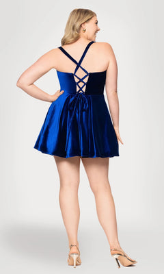 A woman poses with her back to the camera in the Blondie Nites 4469BNW short plus-size prom dress, featuring crisscross straps and a bow, styled with nude heels.
