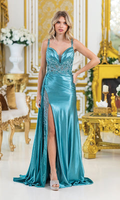 A woman wearing the Long Sheer Illusion Prom Dress: Dancing Queen 4470, a shiny teal v-neck gown with a thigh-high slit, stands in an ornate room featuring gold accents and elegant furniture.