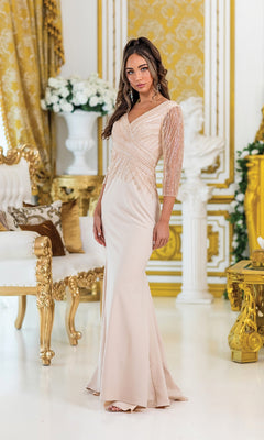 A woman wears the Dancing Queen 4475, a long fitted light pink formal dress with beaded sheer sleeves, standing in an ornate gold and white room.
