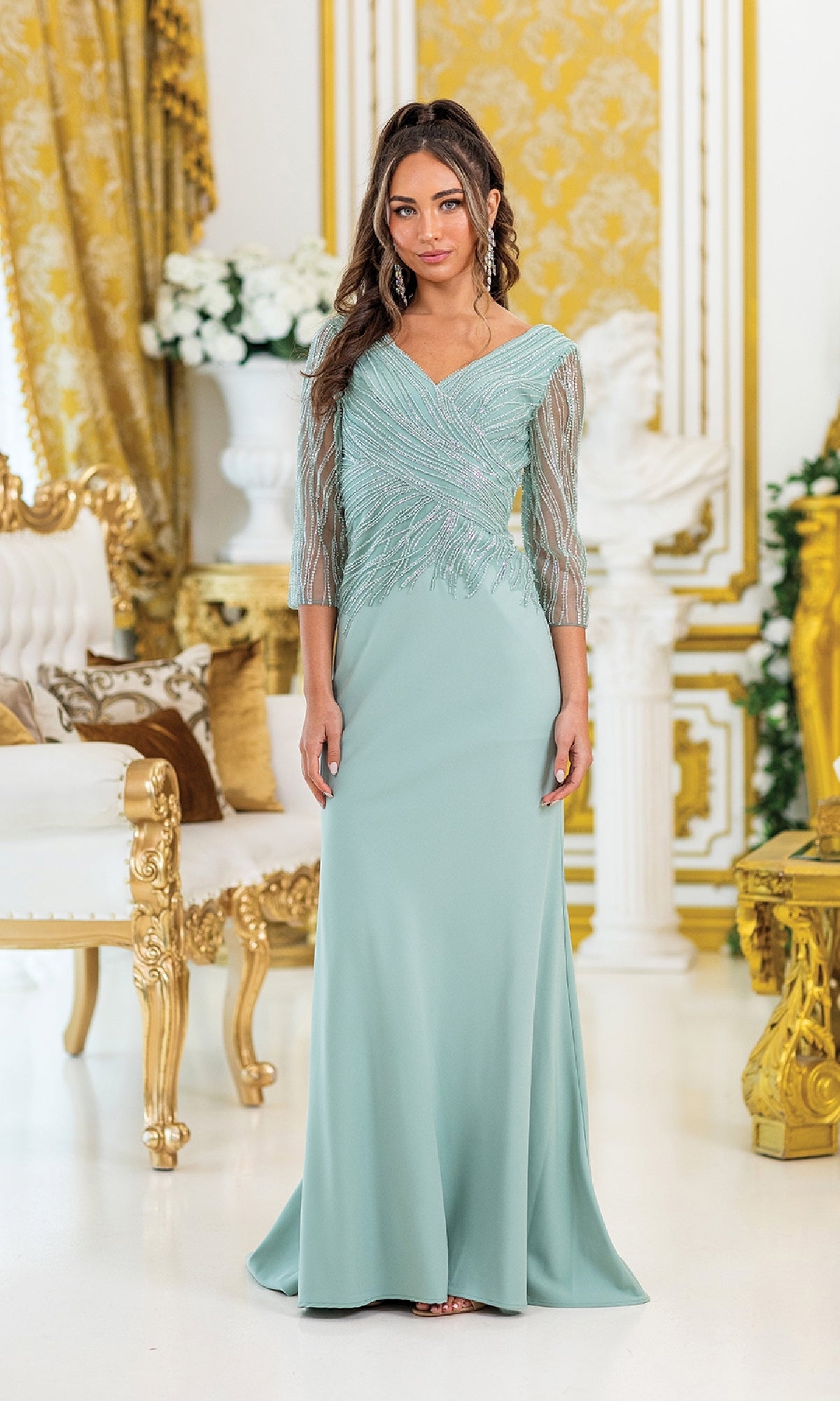 A woman wears the Dancing Queen 4475 Beaded Sleeved Long Formal Dress, featuring a light blue v-neck and sheer beaded sleeves, while standing in an ornate room with gold accents and white floral arrangements.