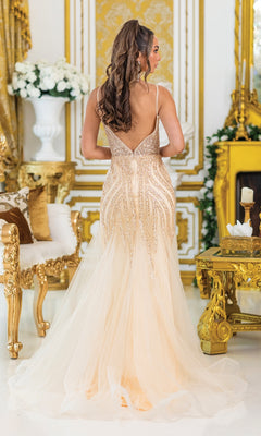 A woman in a Beaded Champagne Prom Dress: Dancing Queen 4488 stands with her back to the camera in a gold-accented room, the gown’s sparkling details elegantly catching the light.
