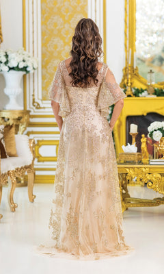 A woman with wavy brown hair stands with her back to the camera, wearing the Dancing Queen 4493 Removable Sleeves Prom Gown in an opulent gold and white room.