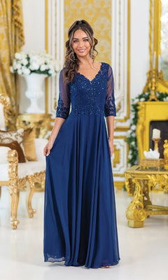 A woman stands in an ornate, gold-accented room wearing the Dancing Queen 4497: a floor-length, navy blue formal dress with lace bodice and sheer long sleeves.