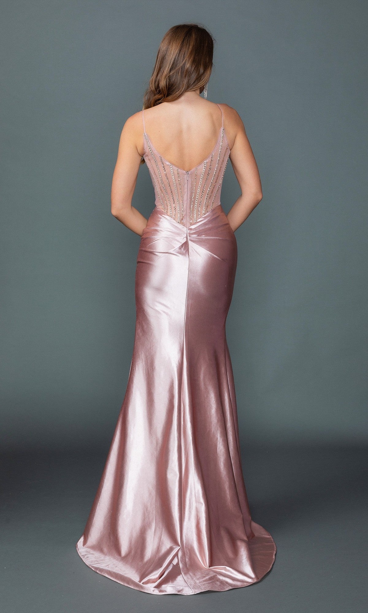 A woman faces away in the Sheer-Corset Long Prom Dress: Dancing Queen 4507, featuring a fitted, floor-length satin skirt, sheer beaded bodice, and thin straps against a plain gray background.