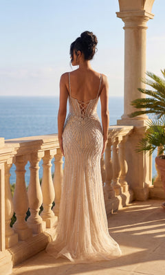 A woman in the Lace-Up Long Beaded Prom Dress: Dancing Queen 4516 with a fitted silhouette and low back stands on a stone balcony overlooking the ocean.