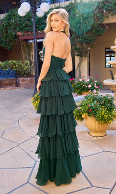 A woman in the Primavera 4530 Long Prom Dress, a strapless dark green gown with a tiered ruffle chiffon skirt, stands outdoors on a stone path surrounded by plants, flowers, and a lamppost, looking over her shoulder.
