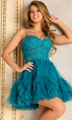 A woman smiles indoors, posing with one hand in her hair while wearing the Jovani 45335 short homecoming dress—a teal, lace-embroidered design featuring spaghetti straps and a ruffled tulle skirt.