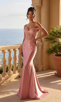 A woman in the Off-Shoulder Mermaid Prom Gown: Dancing Queen 4540, featuring delicate lace detail and a fitted rose gold mermaid skirt, stands on a balcony overlooking the ocean.