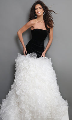 A woman stands against a gray background wearing the Long Formal Dress: Jovani 45670 in Black/Offwhite, which features a strapless velvet fitted bodice and a voluminous white ruffled tulle skirt.