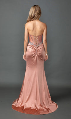 A woman models the Long Prom Dress: Dancing Queen 4570—a strapless satin gown in a fitted blush silhouette with a corset bodice, lace-up back, and ruched detailing—while standing against a plain gray background.