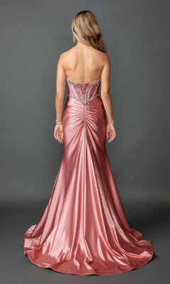 A woman stands facing away, wearing the Long Prom Dress: Dancing Queen 4580—a strapless metallic pink gown with a sleek corset bodice adorned with crystal bead embellishments and jeweled details. The dress features a beautifully gathered train and is set against a plain gray background.