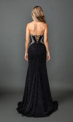 A woman with long, wavy hair is wearing the Dancing Queen 4583 long prom dress—a floor-length black gown featuring sparkly embellishments and a lace-up corset back—as she stands against a plain gray background.