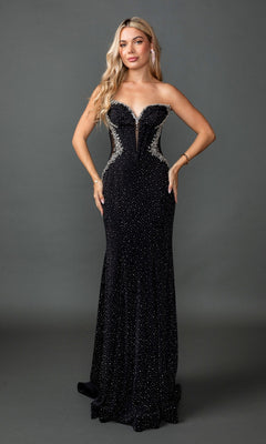 A woman wearing the Long Prom Dress: Dancing Queen 4583, a strapless fitted black gown with silver detailing and sparkly embellishments, stands against a plain gray background. The elegant look is completed by a lace-up corset back.