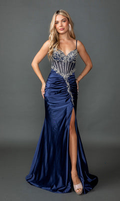 A woman stands against a plain gray background wearing the Long Prom Dress: Dancing Queen 4591 in navy, which features a beaded bodice with crystal-embellished corset detailing, thin straps, a ruched satin fitted sheath skirt with a high slit, and open-toed heels.