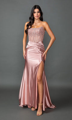 A woman wearing the Long Prom Dress: Dancing Queen 4592 in rose gold, which features a strapless beaded corset bodice and a satin sheath skirt with a high slit, stands against a plain gray background.