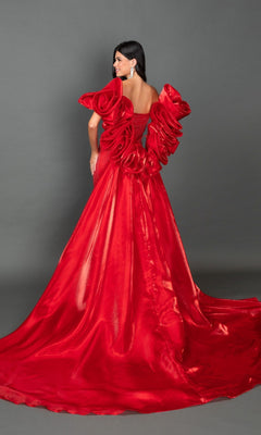 A woman wearing the Long Prom Dress: Dancing Queen 4597 poses against a gray background. The dramatic red gown features striking ruffled shoulder details and an elegant, flowing train, combining the sophisticated allure of a strapless prom dress with the regal charm of a long cape prom dress.