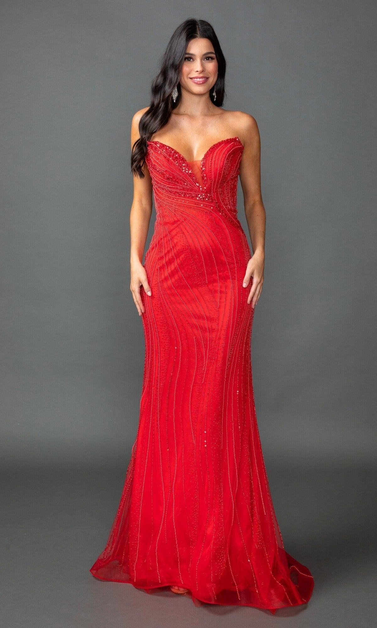 A woman wearing the Long Prom Dress: Dancing Queen 4597 in red, a strapless and fitted evening gown adorned with subtle sparkly embellishments, stands against a plain gray background.