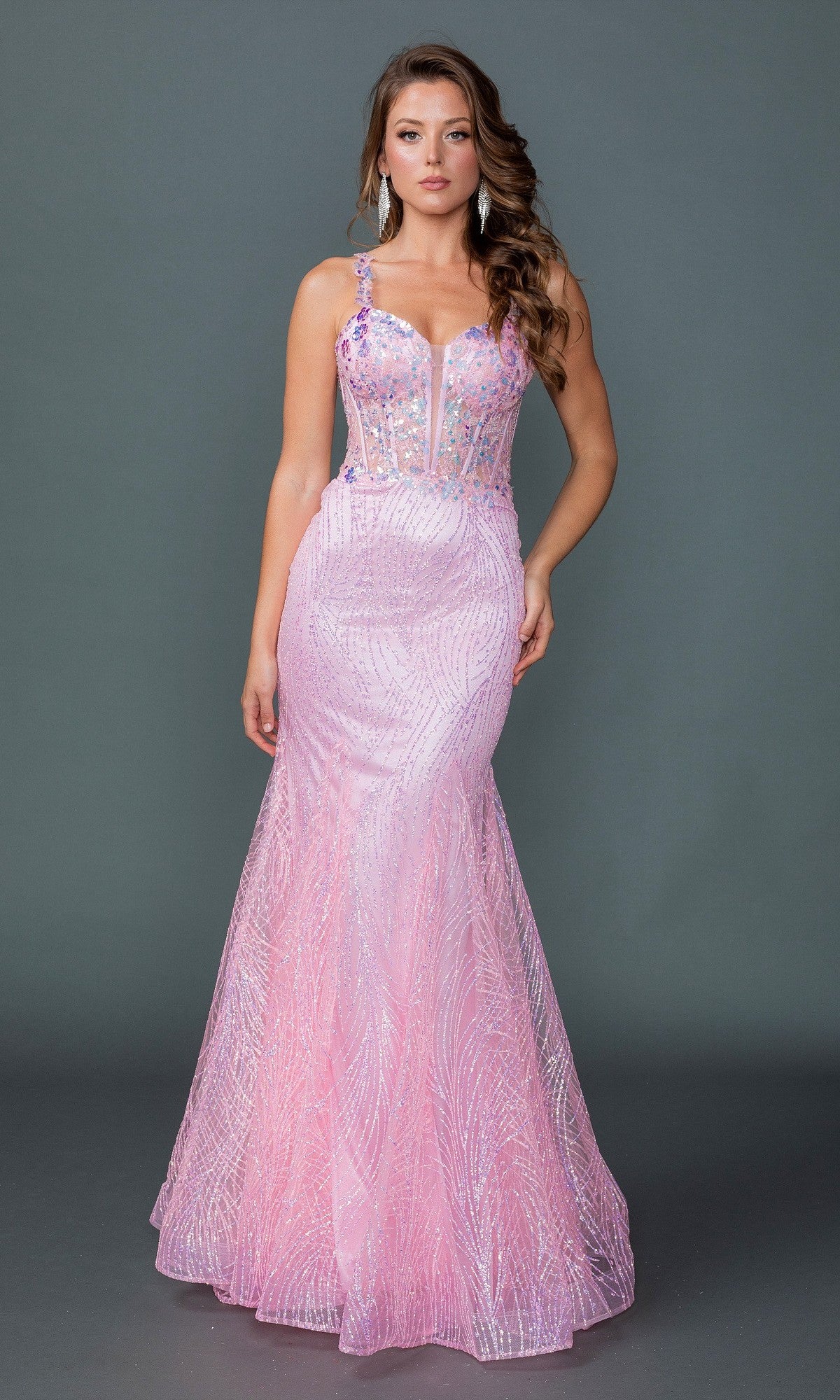 A woman poses against a gray background in the Dancing Queen 4609 long pink prom dress, featuring a fitted mermaid silhouette, sheer corset bodice, and sparkling embellishments.