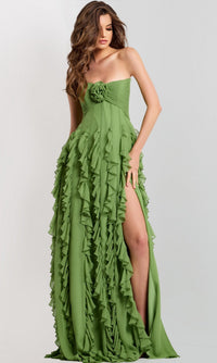 A woman wears the Jovani 46379 Long Prom Dress in light green, with ruffle details, a ruched bodice adorned with a floral accent, and a high slit, posing against a plain backdrop.