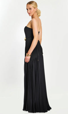 A woman in a strapless black Jovani 47000 floor-length formal dress featuring a pleated skirt and gold floral waist detail, accessorized with gold jewelry, stands against a plain light background.