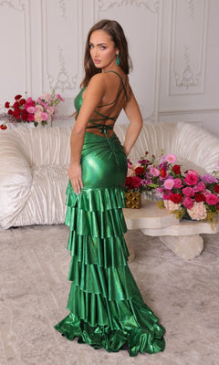 A woman in the Ava Presley 47101 Ruffled Long Shimmer Prom Dress stands before a cream sofa adorned with pink and red floral arrangements in an elegant room.