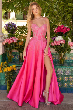 A woman poses before flowers and green tiles, wearing the Ava Presley 47192 long prom dress, a bright pink mikado satin gown with a corset bodice, high slit, and silver high-heeled sandals.