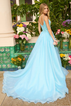 A woman wearing the Ava Presley 47242 long prom dress with a floral beaded bodice and flowing A-line skirt stands outdoors near lush plants and vibrant flowers, looking over her shoulder.