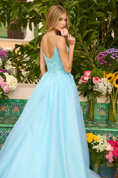 A woman in the Ava Presley 47242 long prom dress with a floral beaded bodice stands outdoors, holding a pink rose to her lips, surrounded by colorful flowers and lush greenery.