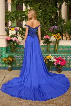 A woman in the Ava Presley 47249 long prom dress, featuring a royal blue chiffon a-line skirt, stands with her back to the camera amid vibrant floral arrangements and green tiled walls.