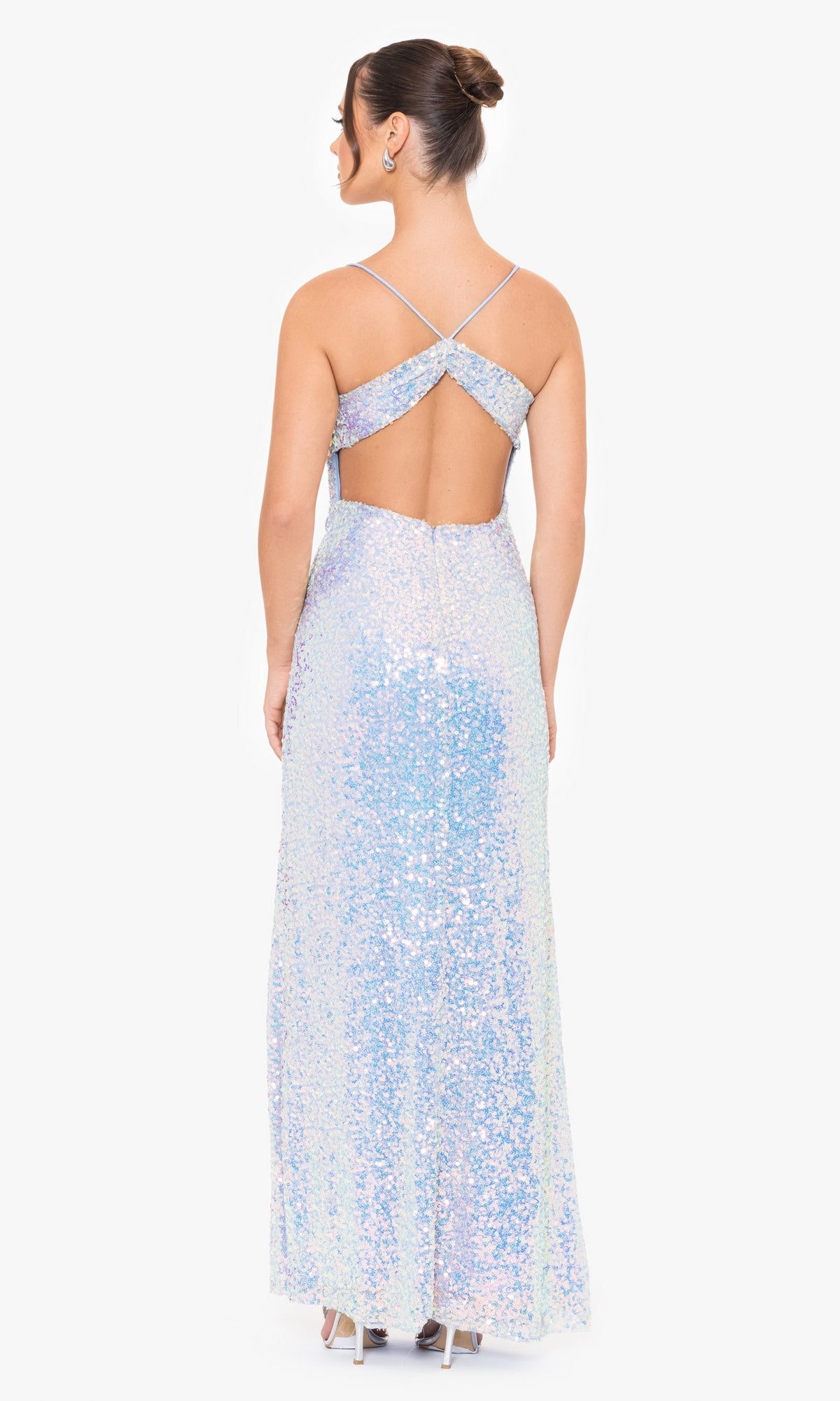 A woman wears the Blondie Nites Long Sequin Prom Dress 4727BN, featuring iridescent sequins, crisscross straps, and an open back, as she stands facing away from the camera.