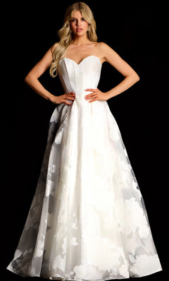 A woman in an off-white Jovani 47327 long prom dress with a corset bodice, strapless sweetheart neckline, and floral details stands against a black background.