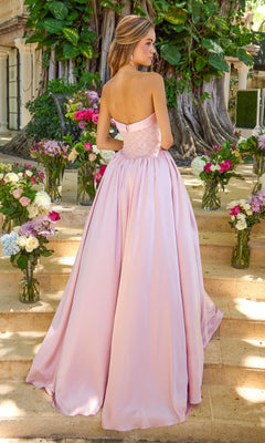 A woman stands on stone steps wearing a light pink, strapless, beaded bodice Ava Presley 47363 ball gown, surrounded by vases of flowers.