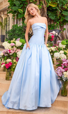 Ava Presley 47374 light blue minimalist prom dress, a strapless floor-length gown with a fitted bodice and a full skirt with pockets, standing among vases of flowers.